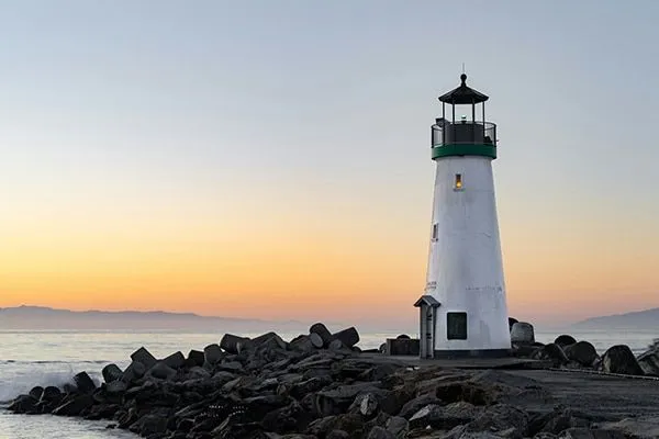 A lighthouse standing at the edge of the water at sunset